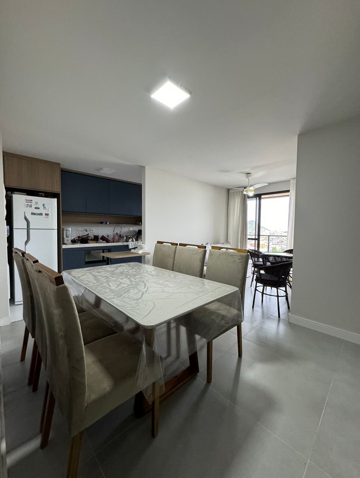 Sala de jantar integrada com cozinha de armários azuis e vista para a varanda.