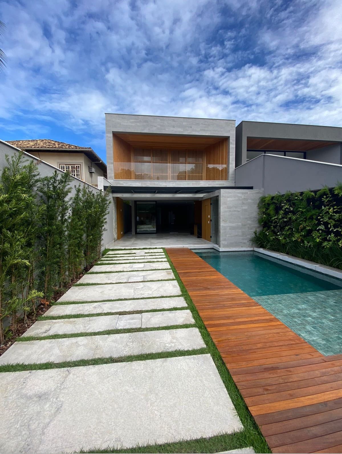 Fachada de casa moderna com piscina, deck de madeira e caminho de pedras no jardim.