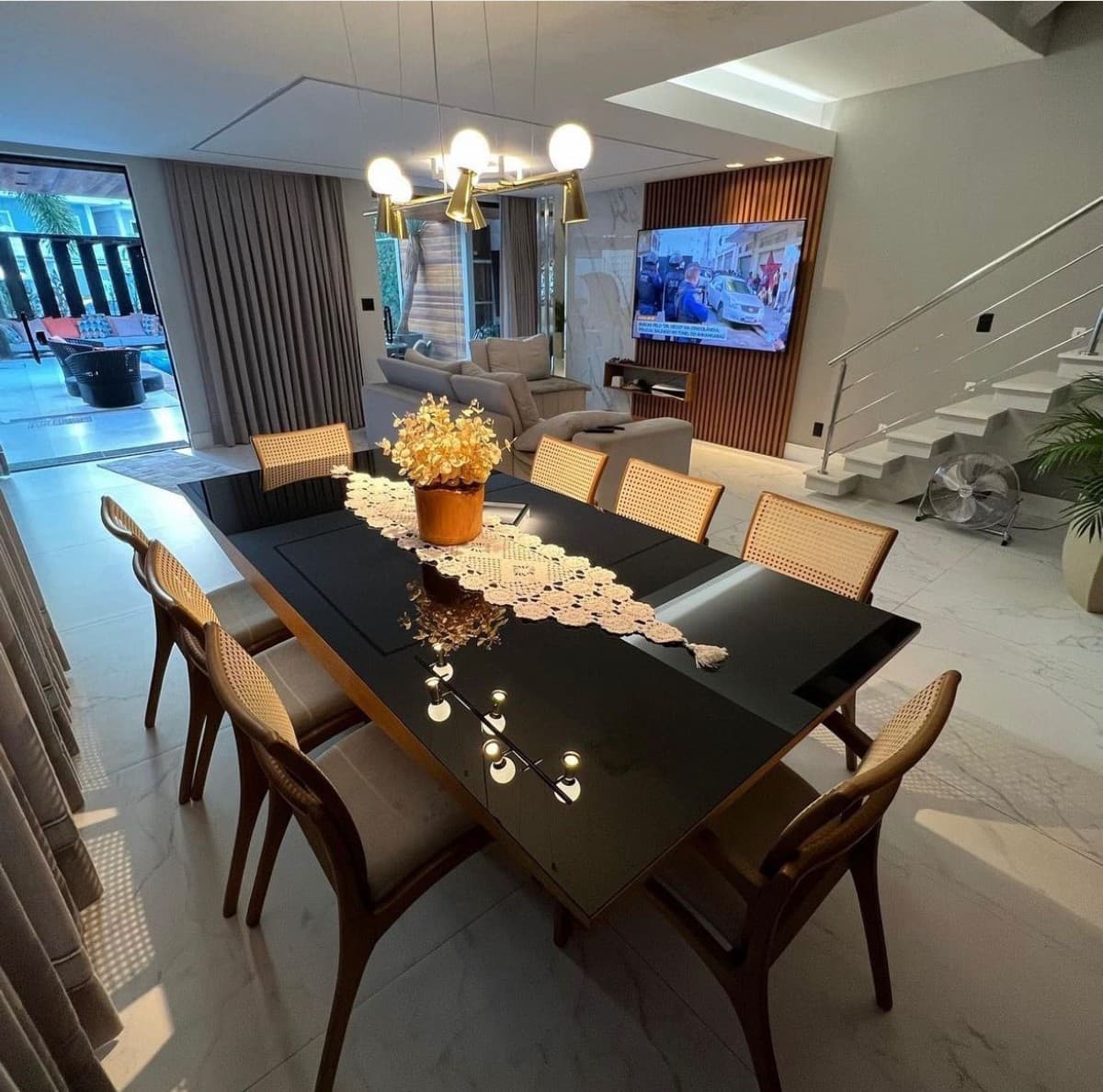 Sala de jantar com mesa preta e cadeiras de palhinha, integrada à sala de estar e escada.