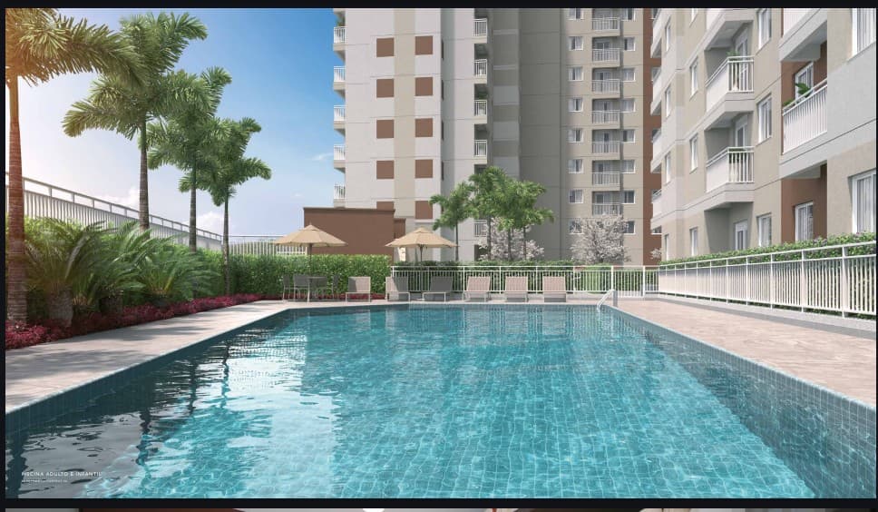 Piscina ao ar livre com deck e espreguiçadeiras cercada por área verde e prédios ao fundo